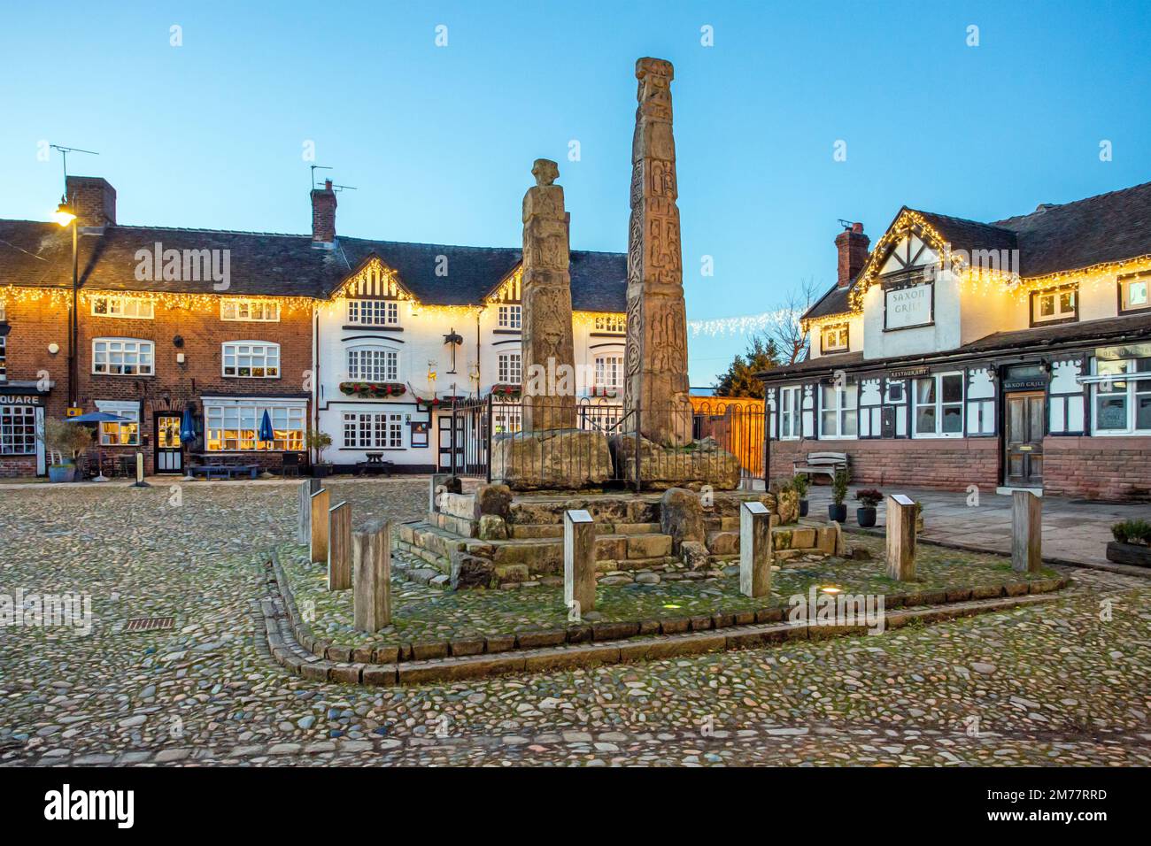 Der mit Flutlicht beleuchtete alte kopfsteingepflasterte Marktplatz in der Cheshire Marktstadt Sandbach mit den sächsischen Kreuzen und zwei alten Trainerhäusern in der Nacht Stockfoto