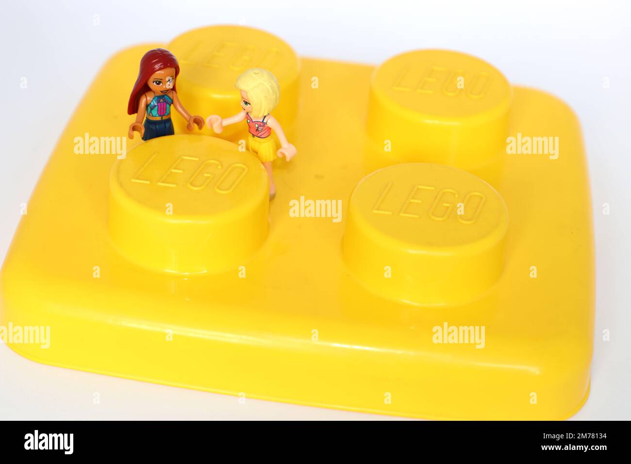 2 Lego-Mädchen halten sich an den Händen und stehen auf einem großen gelben Block Stockfoto