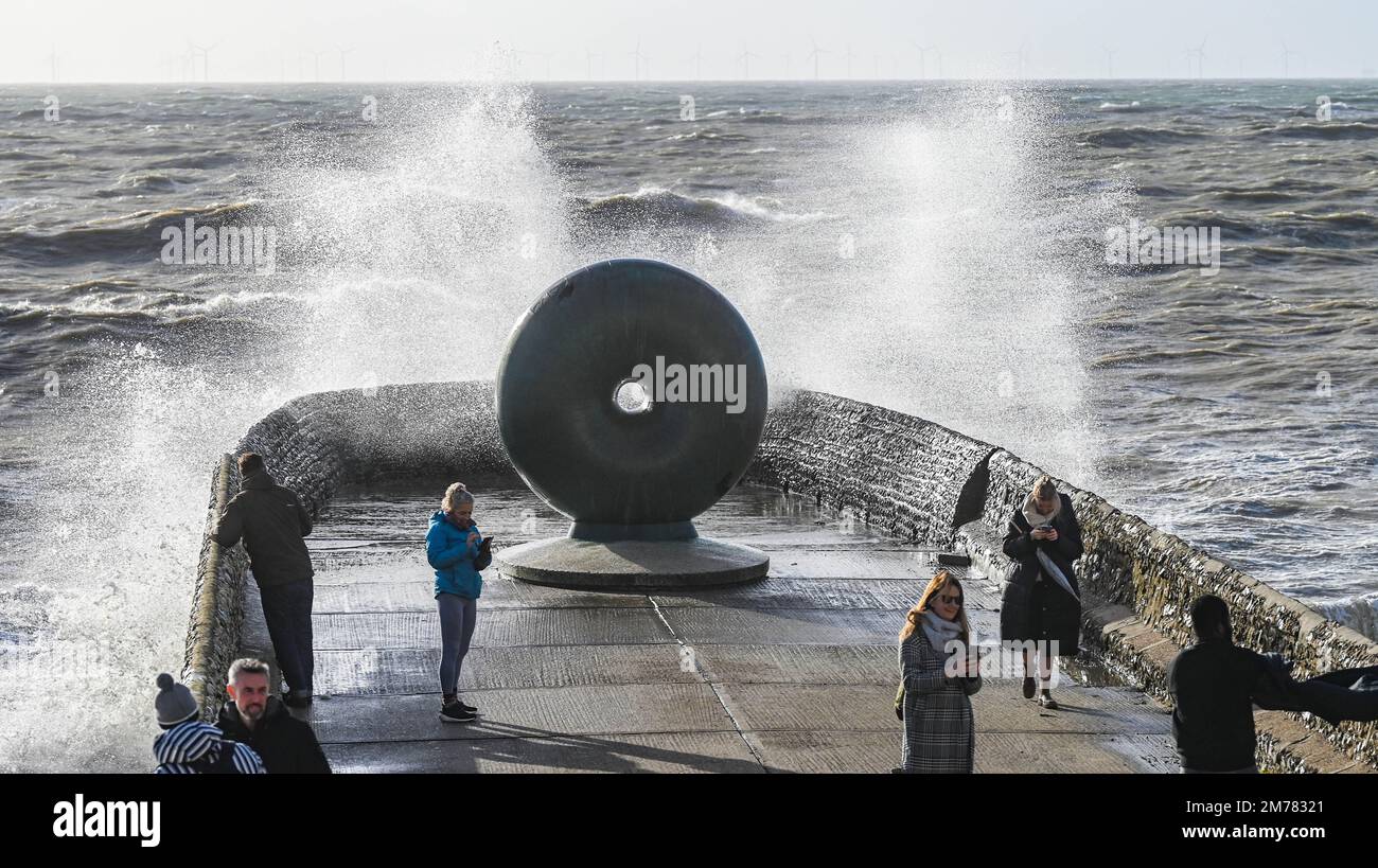 Brighton UK 8. Januar 2023 - Besucher werden nass, wenn sie beobachten, wie die Wellen am Brighton Beach und am Meer an der berühmten Donut-Skulptur einschlagen, während Stürme die Südküste heute mit einer Mischung aus starkem Wind, Sonnenschein und Regen treffen : Credit Simon Dack / Alamy Live News Stockfoto