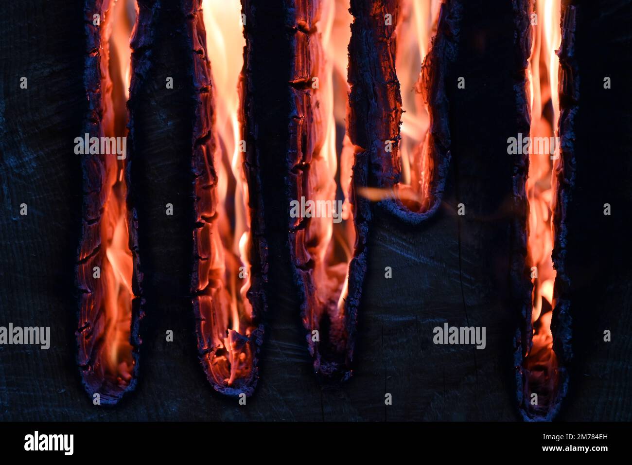 Nahaufnahme leuchtender orangener Flammen, die in Dunkelheit verkohlte Holzlatten verzehren Stockfoto