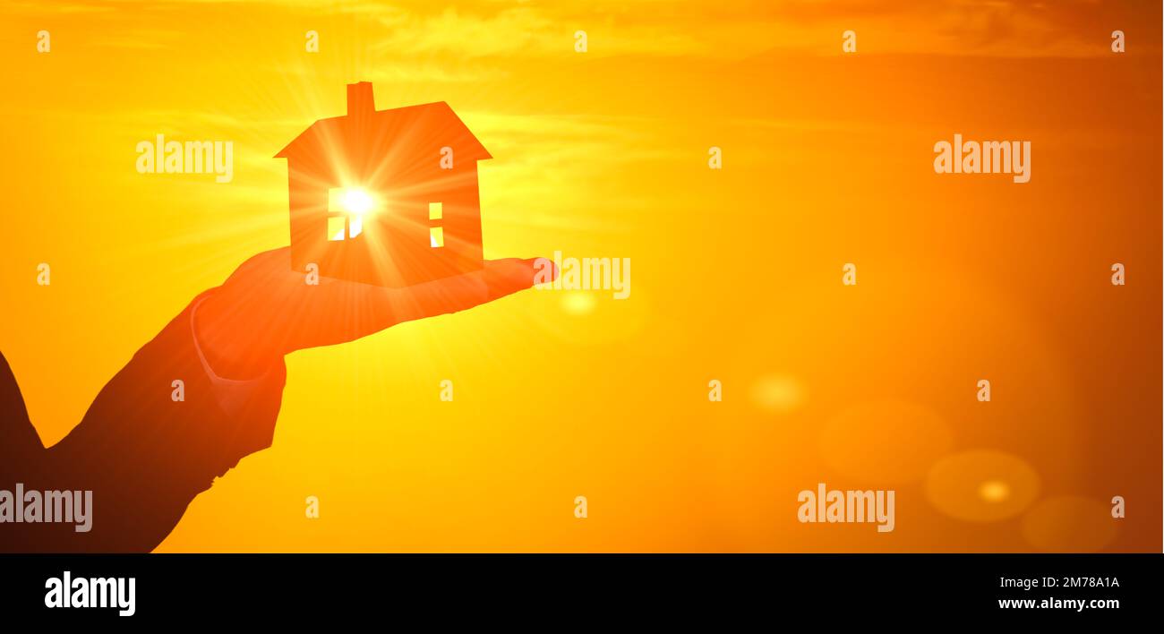 Modell eines Hauses am Abend des Sonnenuntergangs. Silhouettenhaus steht zur Hand. sonnenaufgang-Hintergrund. Immobilienmakler bieten ein neues Haus zum Verkauf oder zur Miete an. Banner Stockfoto