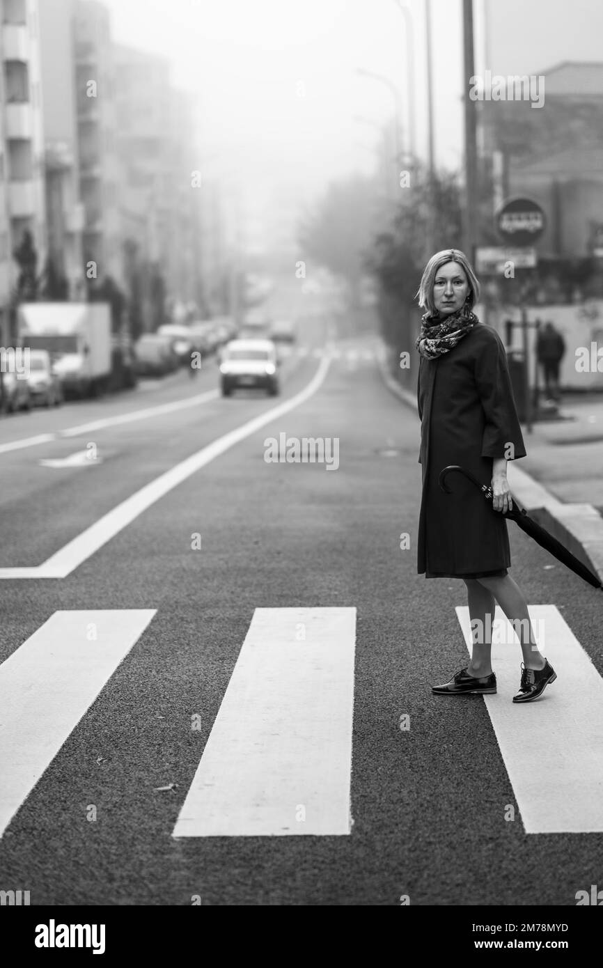 Eine Frau mit Schirm steht im Nebel auf der Straße. Schwarzweißfoto. Stockfoto