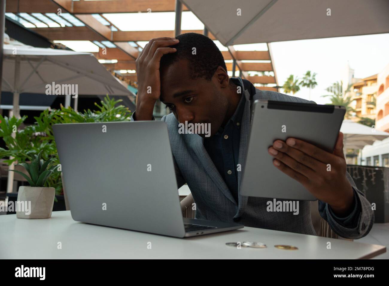 Ein enttäuschter Händler erhält schlechte Nachrichten, wenn er den Markt über sein Tablet und sein Notebook überwacht Stockfoto