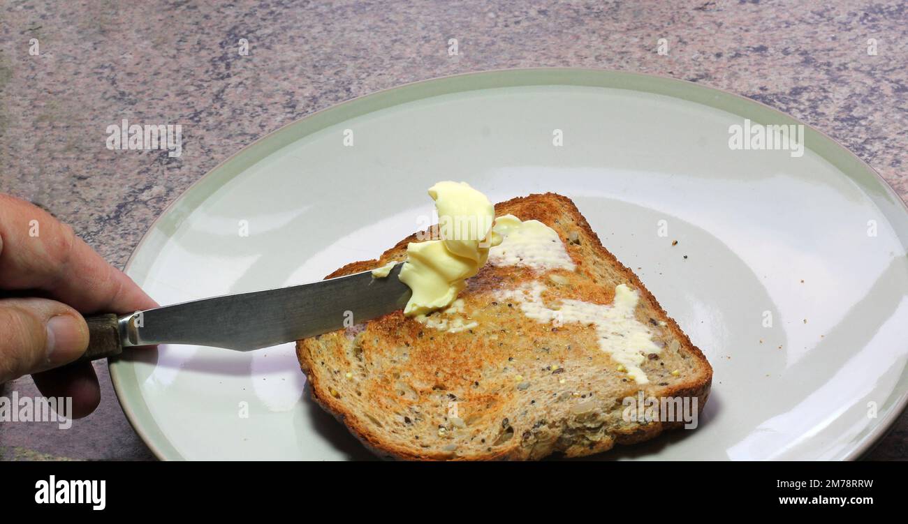 Buttertoast. Halten Sie das Messer mit der Hand fest, um Butter auf ein Stück Toast zu streuen. Stockfoto