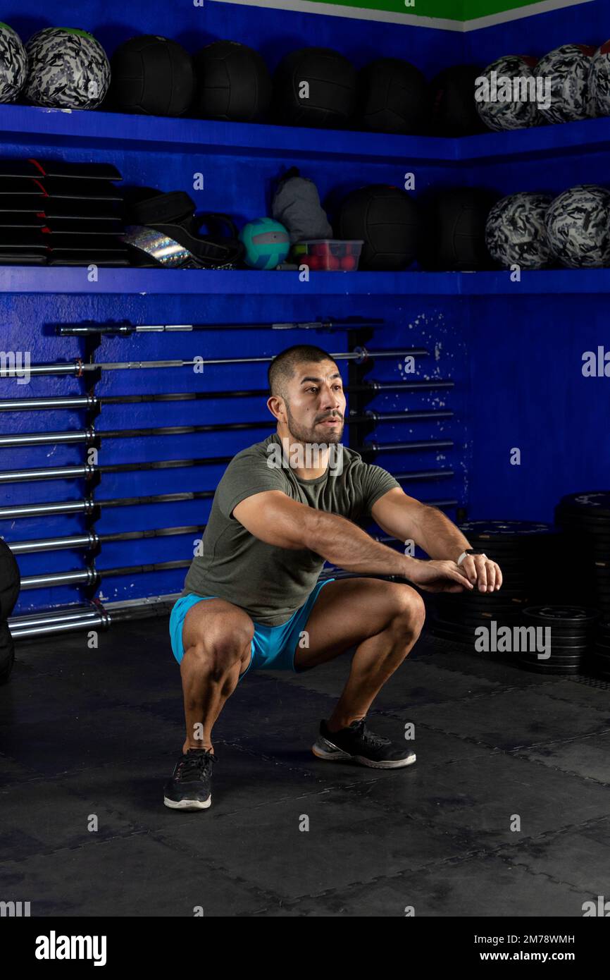 Vertikales Bild eines lateiners, der Kniebeugen macht, Sportbekleidung in einem Crossfit-Gym trägt Stockfoto