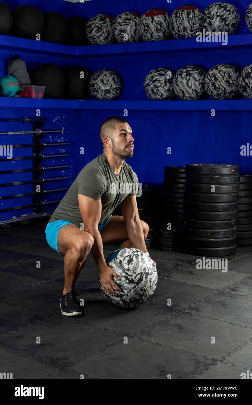 Ein lateinischer Mann, der im Fitnessstudio trainiert und einen Medizinball benutzt Stockfoto