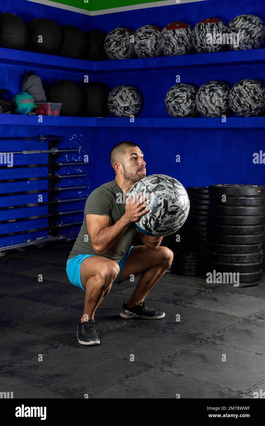 Ein lateinischer Mann, der im Fitnessstudio trainiert und einen Medizinball benutzt Stockfoto