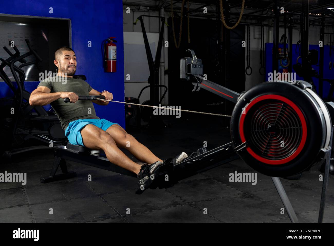 Seitenansicht eines Lateiners mit Sportbekleidung, der in einem Crossfit-Fitnessstudio auf einer Maschine rudert Stockfoto