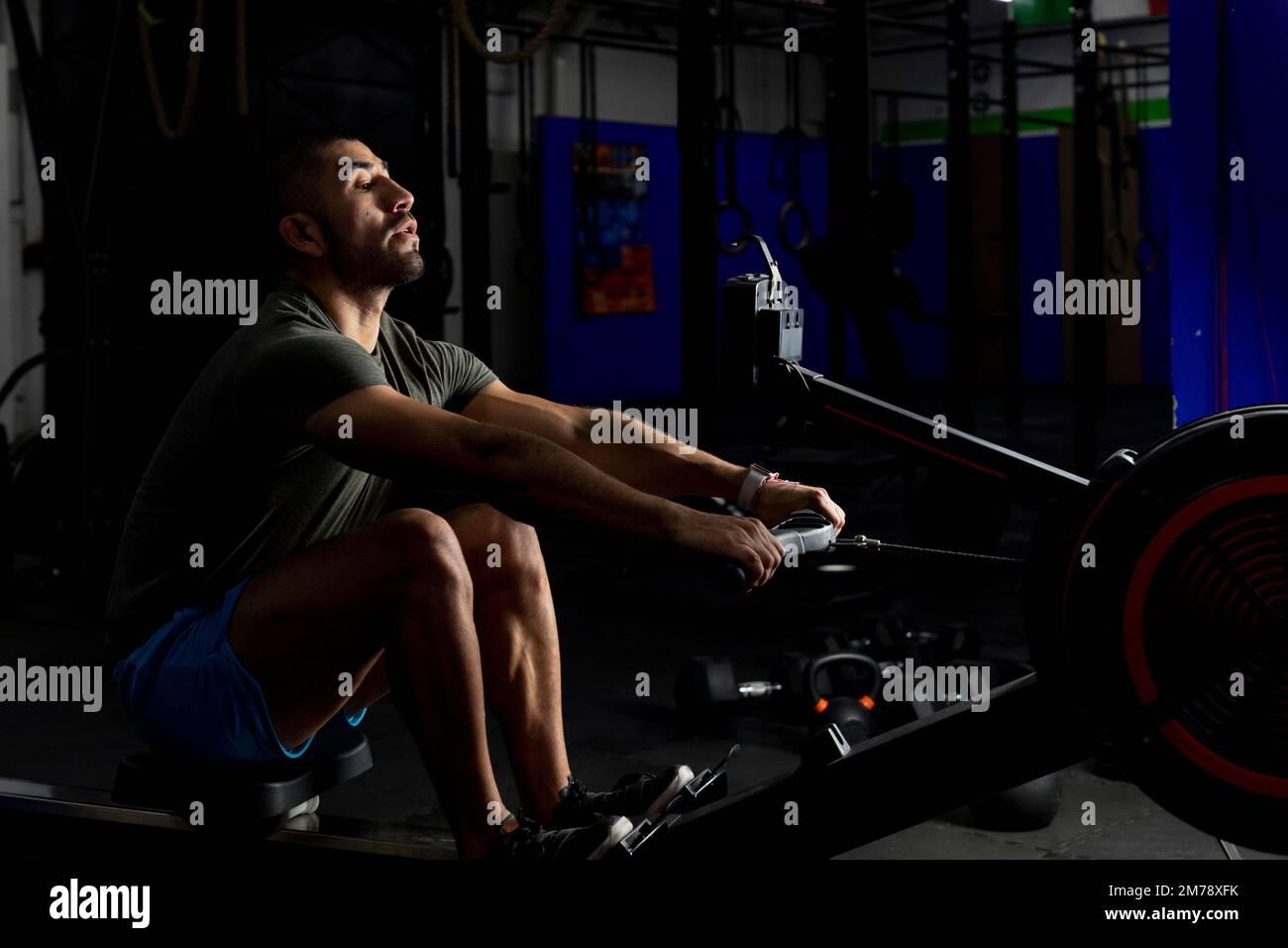 Aufnahme eines Athleten bei schwachem Licht, der in einem Fitnessstudio rudert Stockfoto