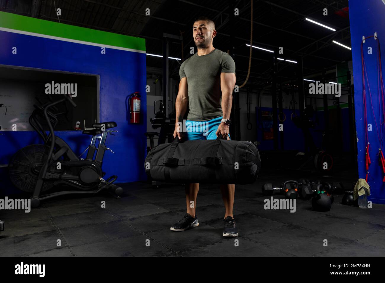 Männlicher Sportler, der Sportbekleidung trägt, in einem Fitnessstudio steht und einen Sandsack hält Stockfoto