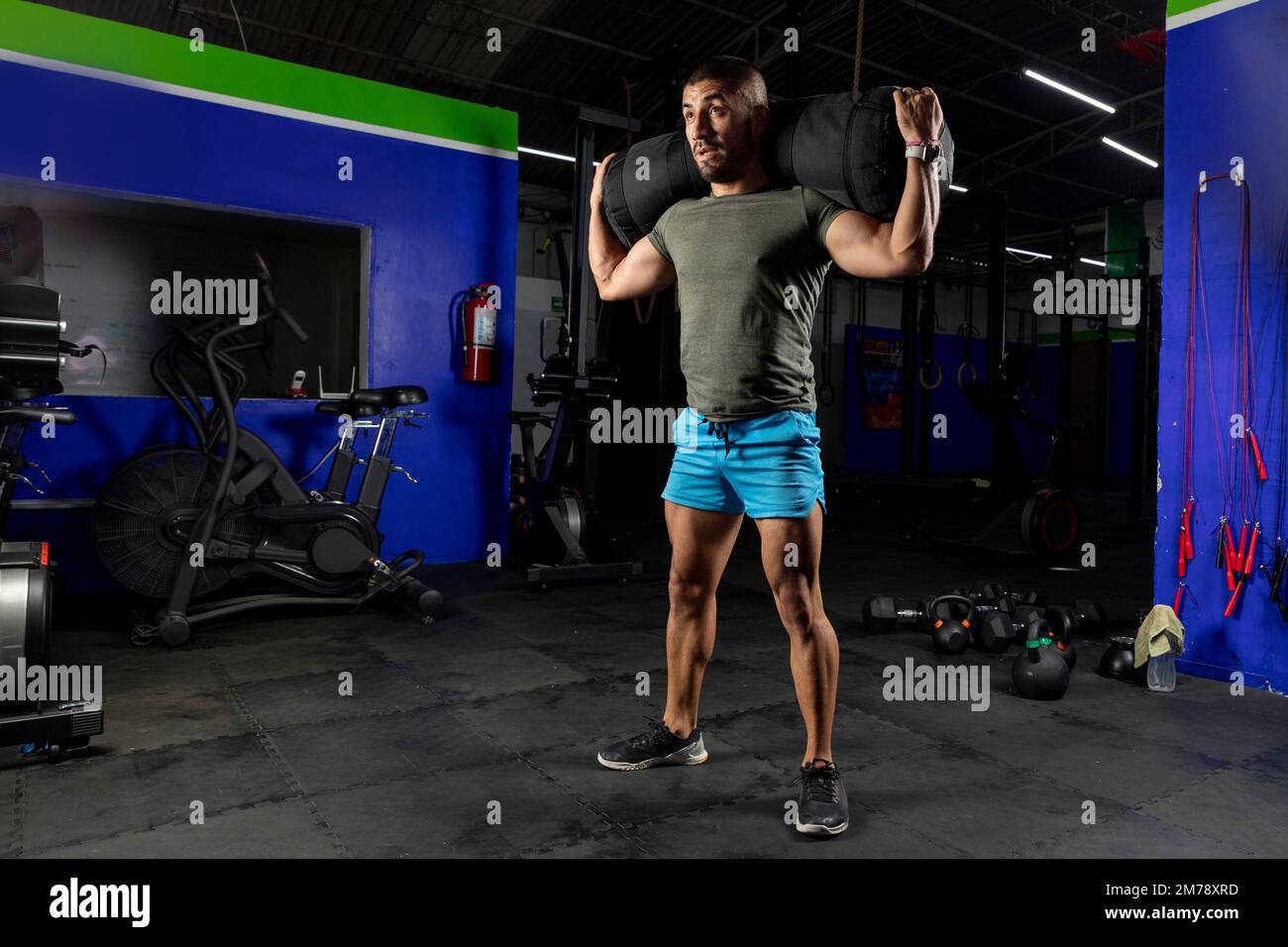 Ein Lateiner mit Sportbekleidung, der beim Training im Fitnessstudio einen Sandsack auf dem Rücken trägt Stockfoto