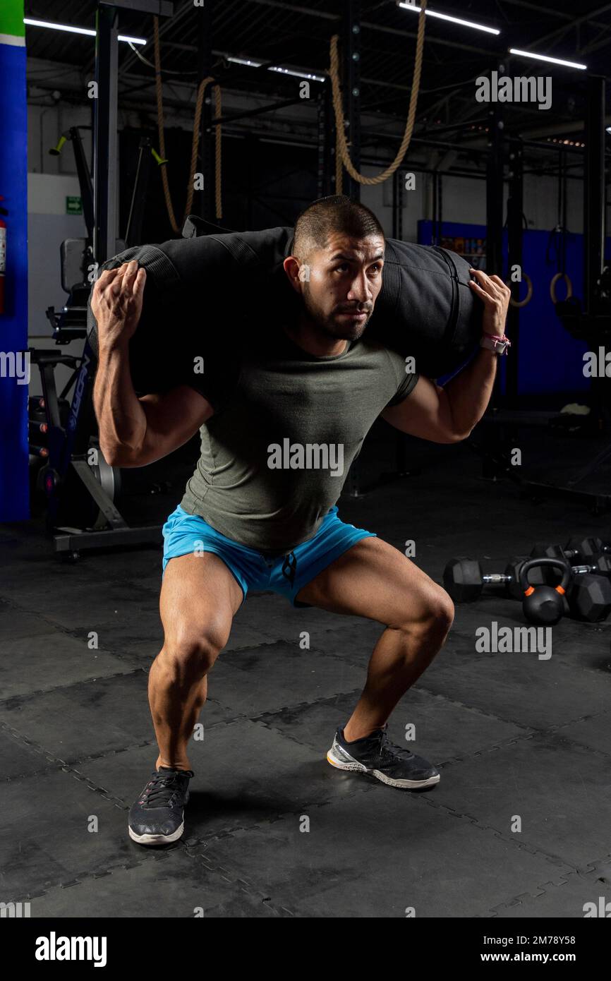 Ein Mann in Sportbekleidung in einem Fitnessstudio, der Squats mit einem Sandsack auf dem Rücken macht Stockfoto