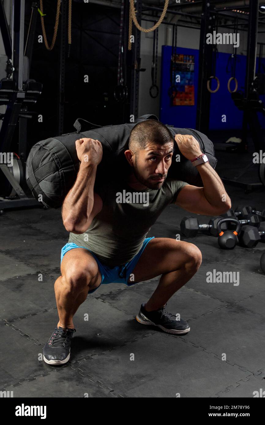 Ein Mann in Sportbekleidung in einem Fitnessstudio, der Squats mit einem Sandsack auf dem Rücken macht Stockfoto