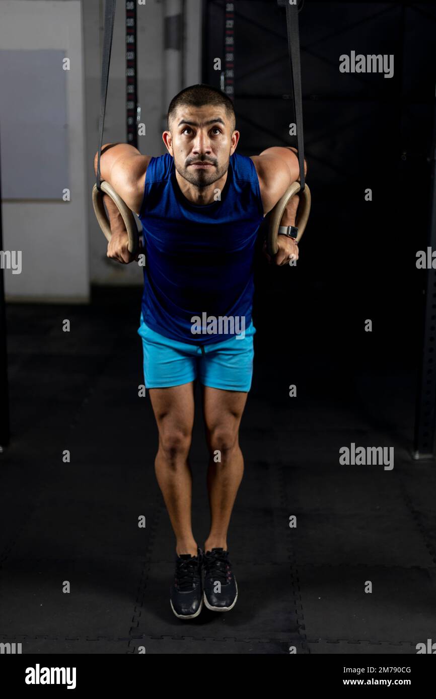 Ein Latino in Sportbekleidung, der Gymnastikübungen an einigen Ringen in einem Fitnessraum macht Stockfoto
