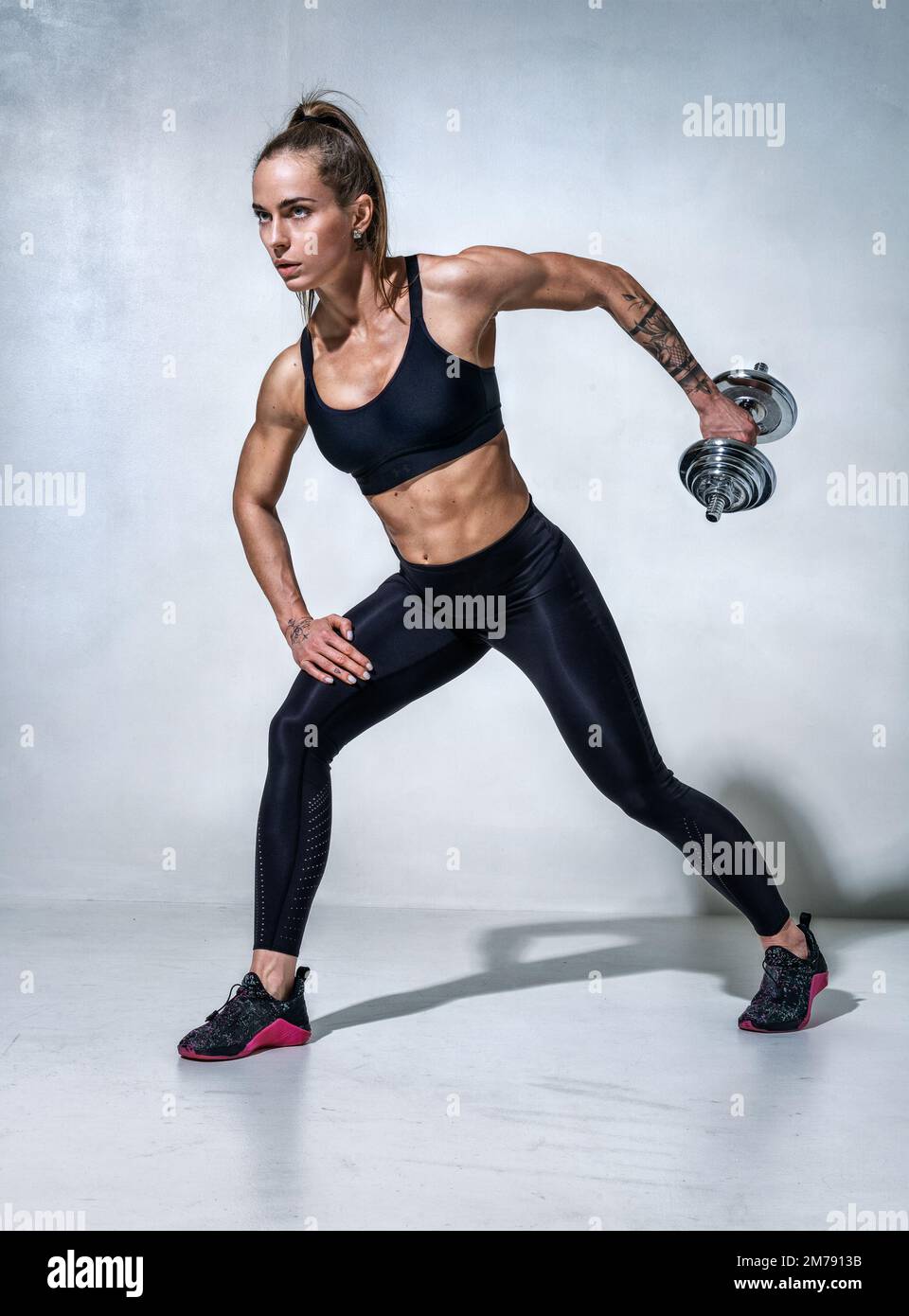 Sportliche Frau, die mit Kurzhanteln trainiert. Foto des Modells in schwarzer Sportbekleidung auf grauem Hintergrund. Sportliche Motivation und gesunder Lebensstil Stockfoto