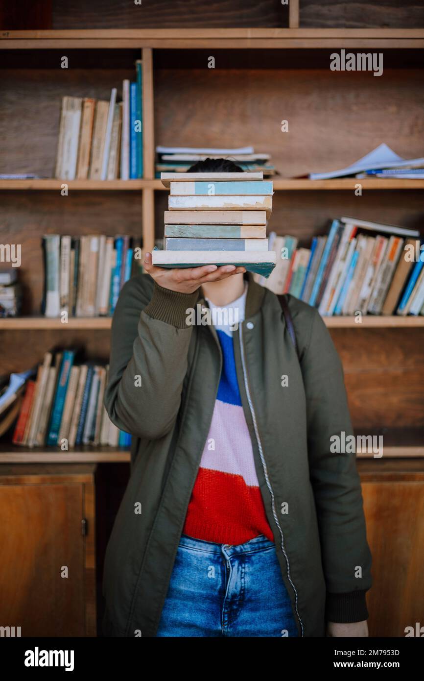 Eine Frau hält einen Stapel Bücher vor einem Regal mit gespendeten Büchern, die von den Interessierten gelesen werden sollen. Wiederverwendung von Büchern durch Antiquitätengeschäfte. Stockfoto