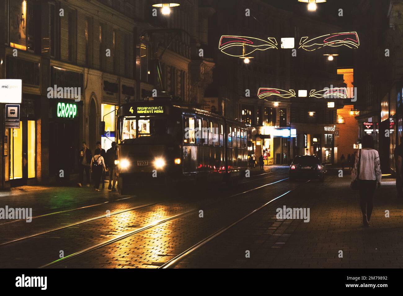 Nachtfoto der Stadt Brünn mit vorbeifahrendem Auto und Straßenbahn, Leute zu Fuß Stockfoto