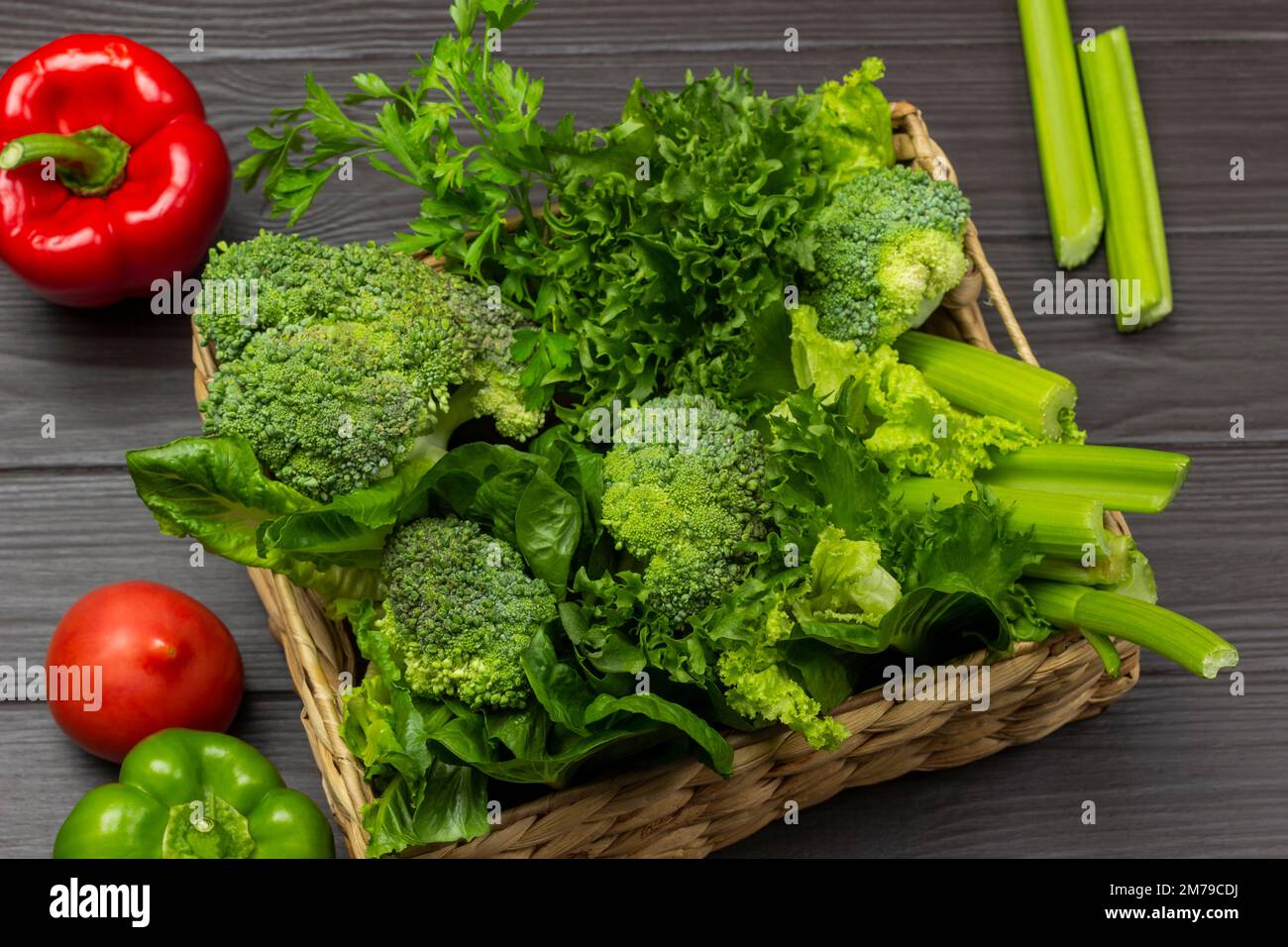 Grünes Gemüse in einem Korb. Tomaten und Paprika auf dem Tisch. Draufsicht. Dunkler Holzhintergrund. Stockfoto