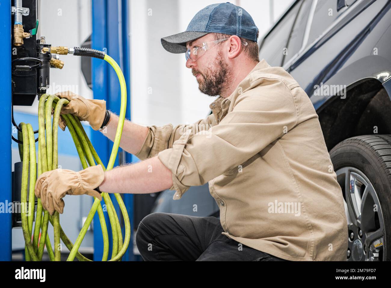 Kaukasischer Mechaniker mittleren Alters, der nach saisonalen Veränderungen Kompressorkabel zum Aufpumpen der Fahrzeugreifen verwendet. Professionelle Autowartungsstation. Stockfoto