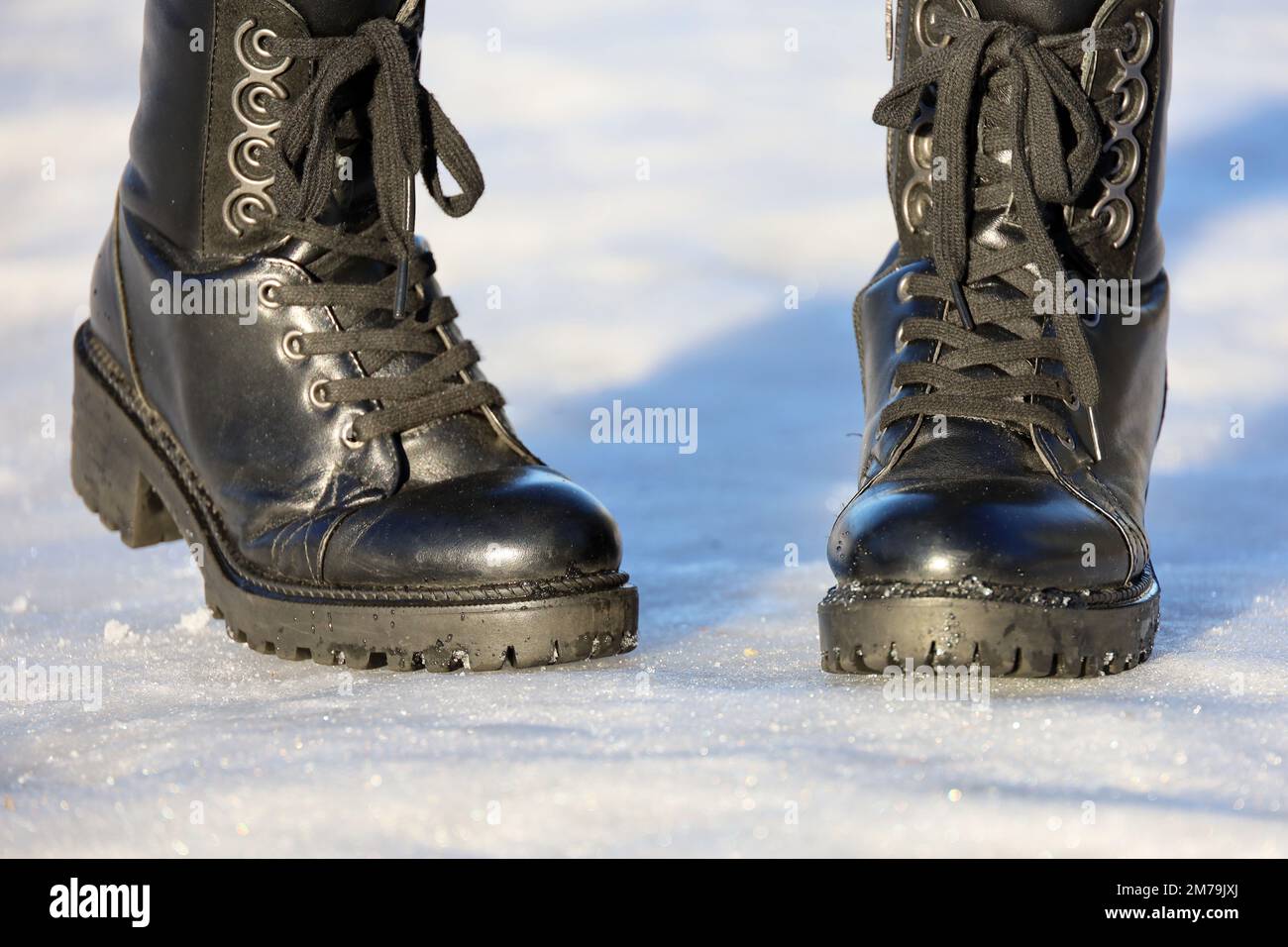 Weibliche Beine in schwarzen Leder Schnürstiefeln auf Schnee. Frau, die auf der Winterstraße läuft, warme Schuhe für kaltes Wetter Stockfoto