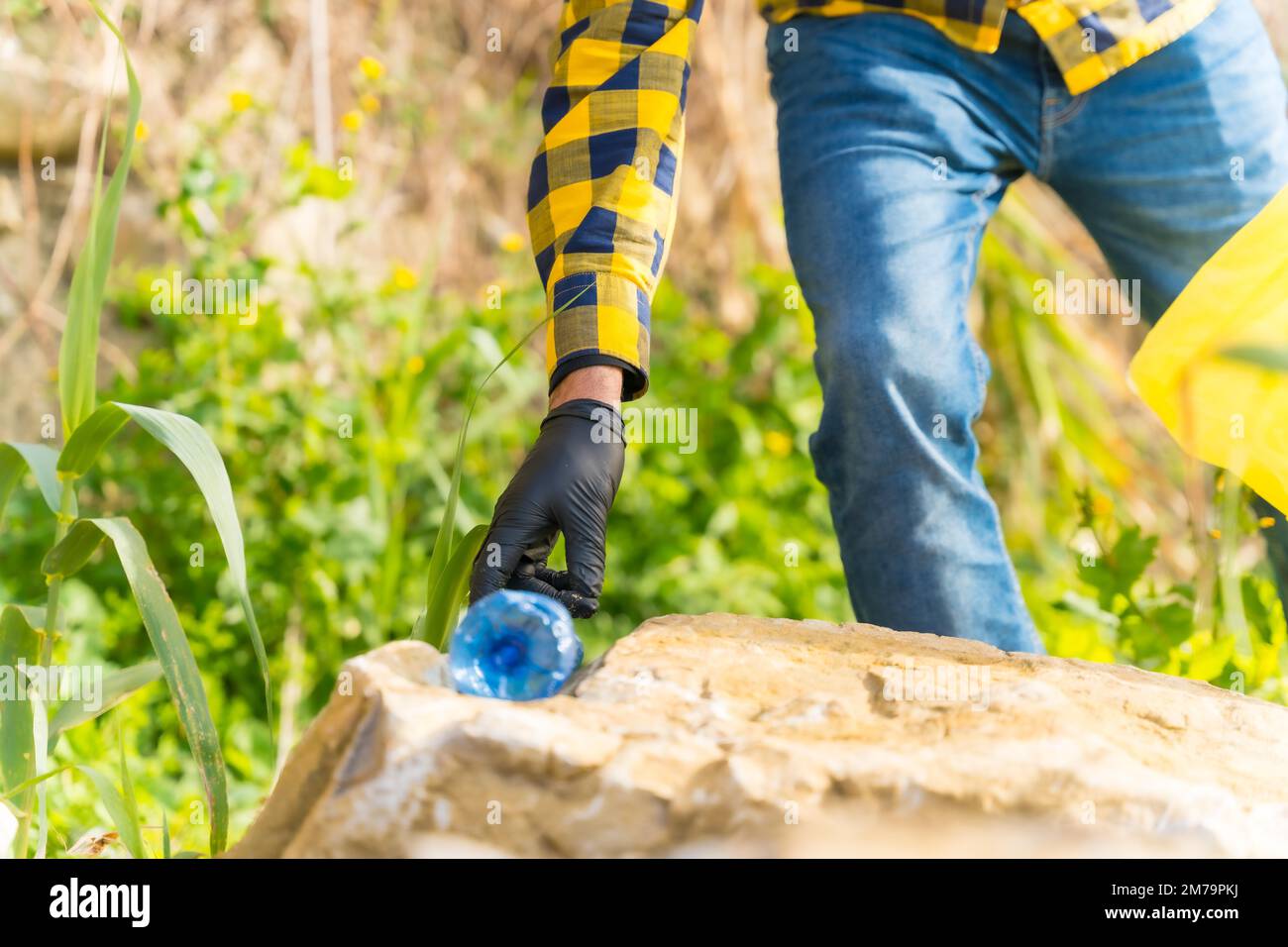 Die Hand eines unbekannten Mannes, der eine Plastikflasche in einem Wald aufhebt. Umweltkonzept, Recycling Stockfoto