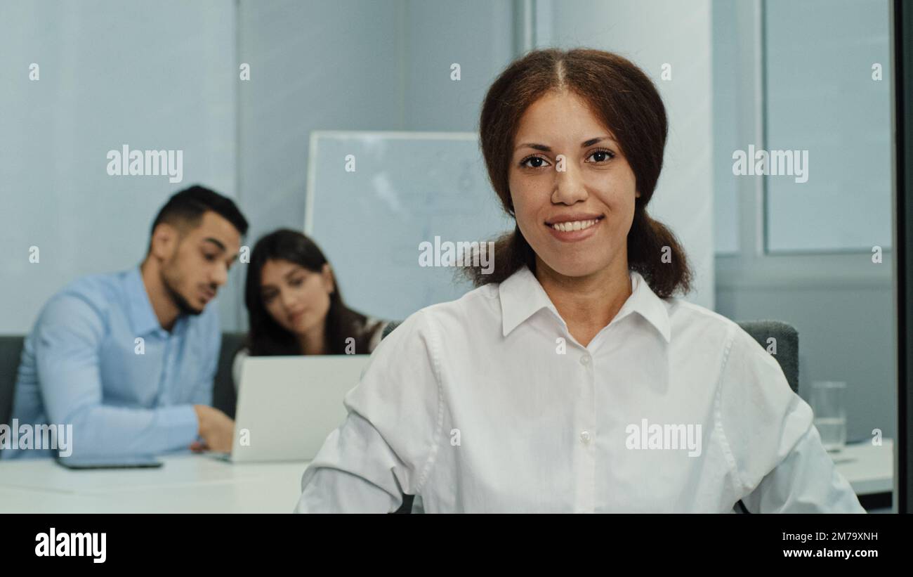 Porträt lächelnde, attraktive Geschäftsfrau, die in einem modernen Geschäftsbüro mit einem Team aus multikulturellen Profis sitzt und in die Kamera schaut. Freundliche Std Stockfoto