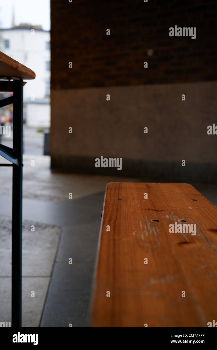 Holzbank und Tischbein aus Metall mit unscharfem Hintergrund und Vordergrund in überdachter Stadtstraße Stockfoto