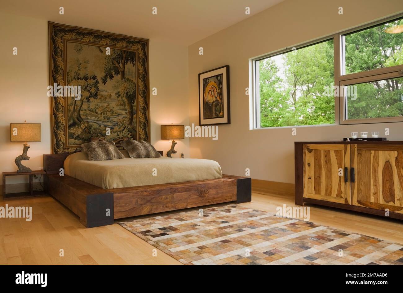 Kingsize-Bett mit Holzrahmen im Hauptschlafzimmer mit Flickwerk-Motiven Teppich im oberen Stockwerk im luxuriösen, modernen kubistischen Stil Haus. Stockfoto