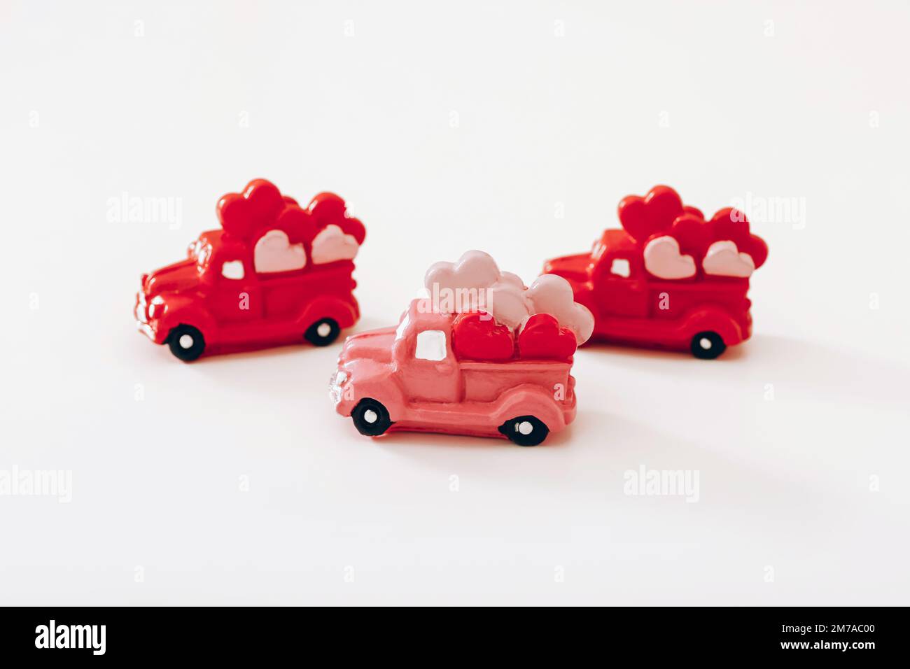 Drei rote Miniaturautos mit Herzen auf weißem Hintergrund. Valentinstag Stockfoto