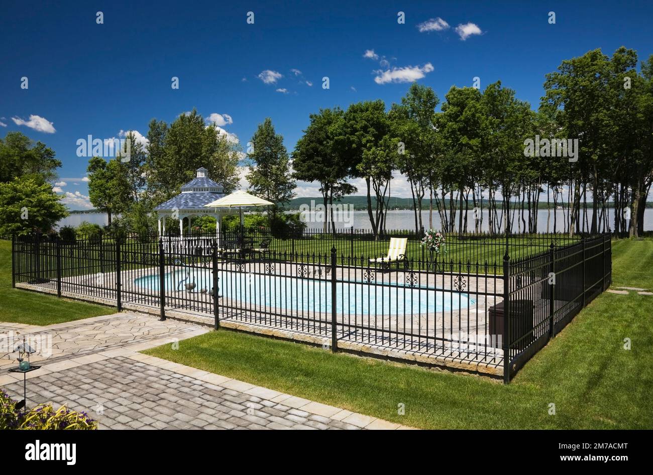 Im Sommer befindet sich ein Swimmingpool im Freien, der von einem schwarzen schmiedeeisernen Zaun umgeben ist. Stockfoto