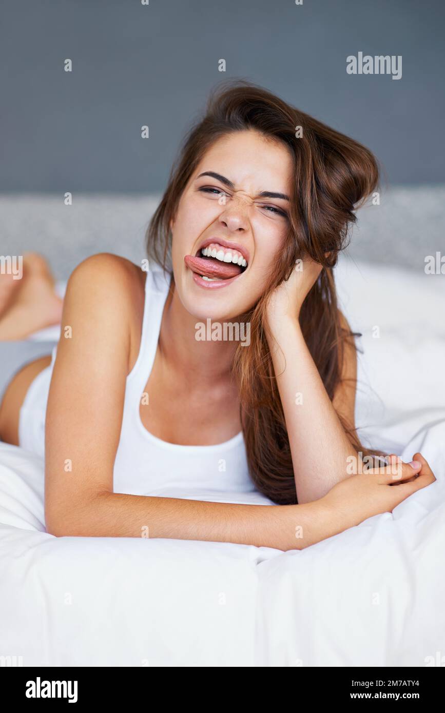 Nichts geht über ein bisschen Morgendummheit. Eine junge Frau, die im Bett liegt und Gesichter zieht. Stockfoto