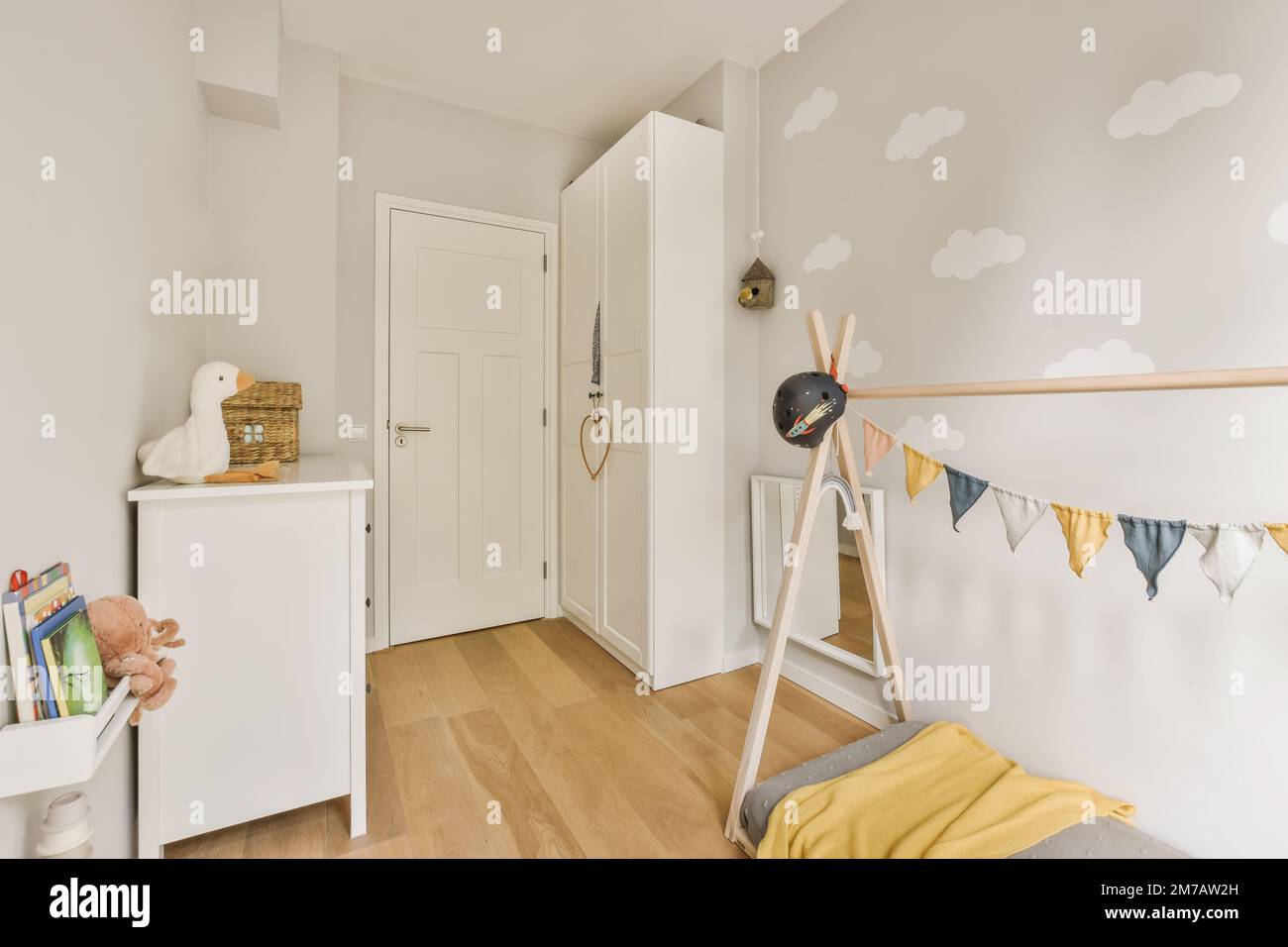 Ein Kinderzimmer mit weißen Wänden und Holzfußboden, eine gelbe Decke auf dem Bett vor der Tür Stockfoto