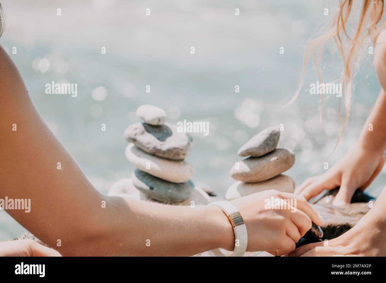 Eine Frau mit Tochter hat eine Biltsteinpyramide am Meer an einem sonnigen Tag auf blauem Meereshintergrund. Frohe Familienferien. Kieselstrand, ruhiges Meer. Konzept Stockfoto