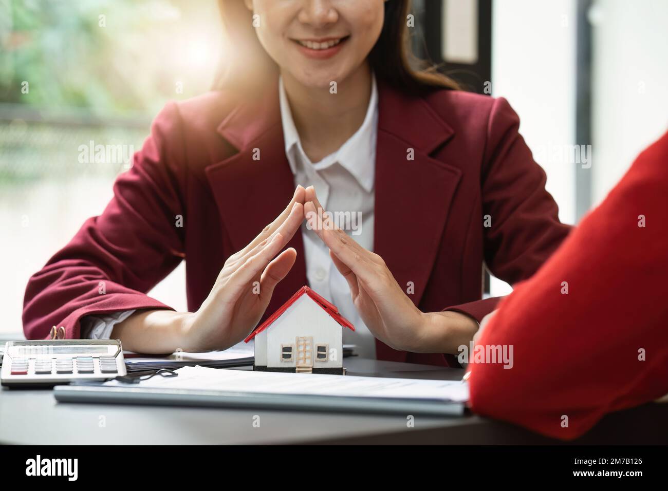 Immobilienkonzept, Agent mit Haus. Haus zur Hand. Sachversicherungs- und Sicherheitskonzept. Die Schutzgeste der Frau und das Symbol des Hauses Stockfoto
