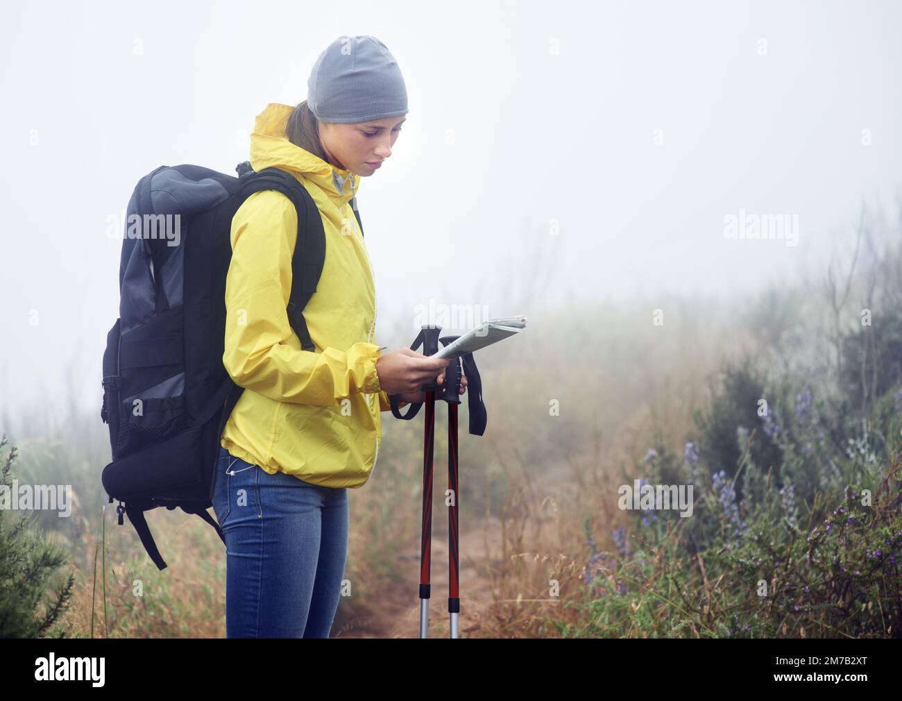 Ich will mich bei diesem Wetter nicht verirren. Eine junge Wanderin, die auf einem Wanderweg auf ihrer Karte nachsieht. Stockfoto