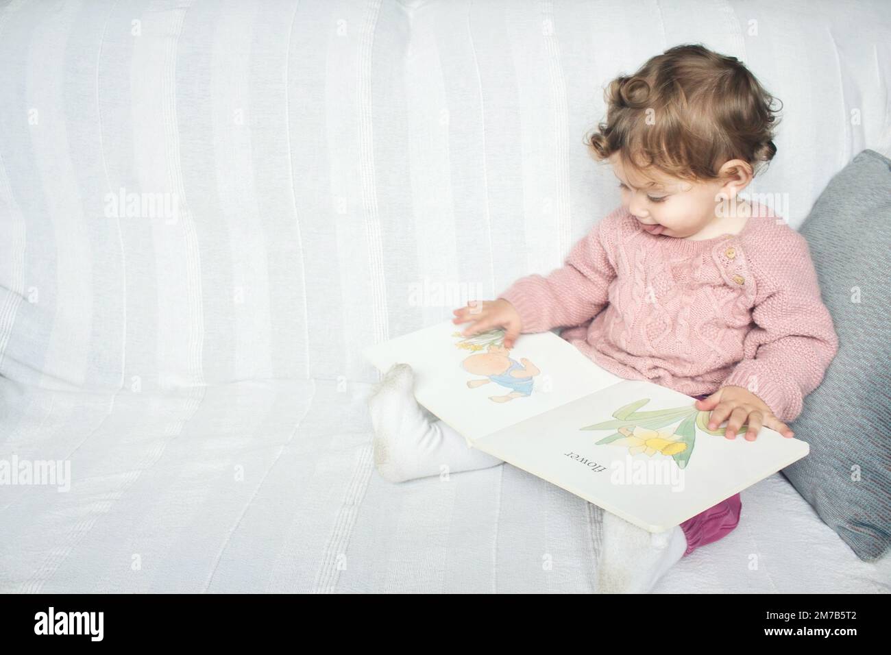 Ein süßes, kleines, weißes Mädchen saß auf dem Sofa und las ein Kinderalbum Stockfoto
