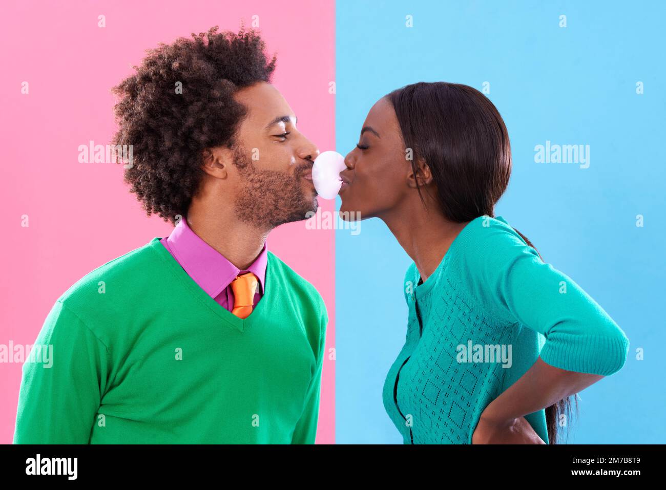 Doppelblase-Liebe. Ein niedliches, stilvolles Paar, das vor einem bunten Hintergrund mit Kaugummi bläst. Stockfoto