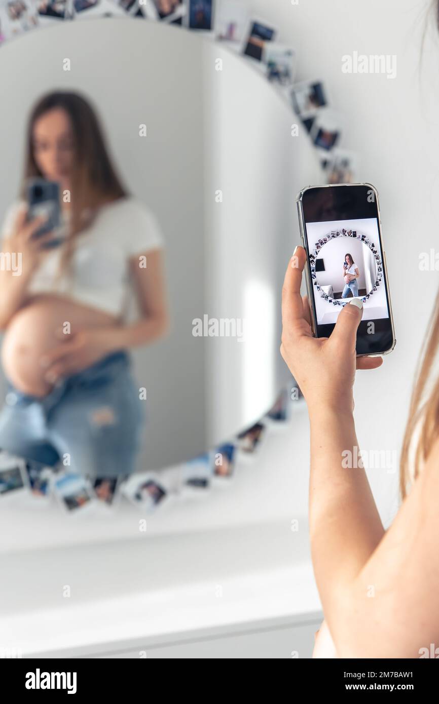 Eine schwangere Frau macht ein Selfie im Spiegel, das Konzept, ein Baby zu erwarten. Stockfoto