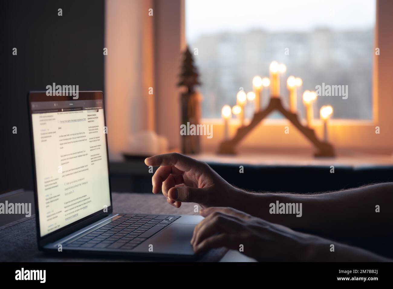 Ein Mann liest die Nachrichten, während er nachts vor einem Laptop-Bildschirm sitzt. Stockfoto