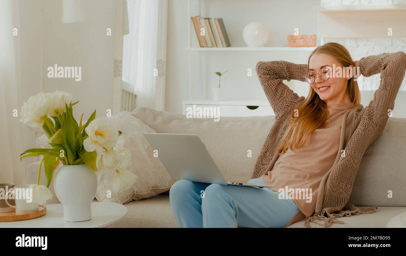 Weiße glückliche erfolgreiche Gewinnerin Frau mit Brille Mädchen Frau feiern Leistung erstaunliches Ergebnis auf der Apartmentcouch mit Laptop App Stockfoto