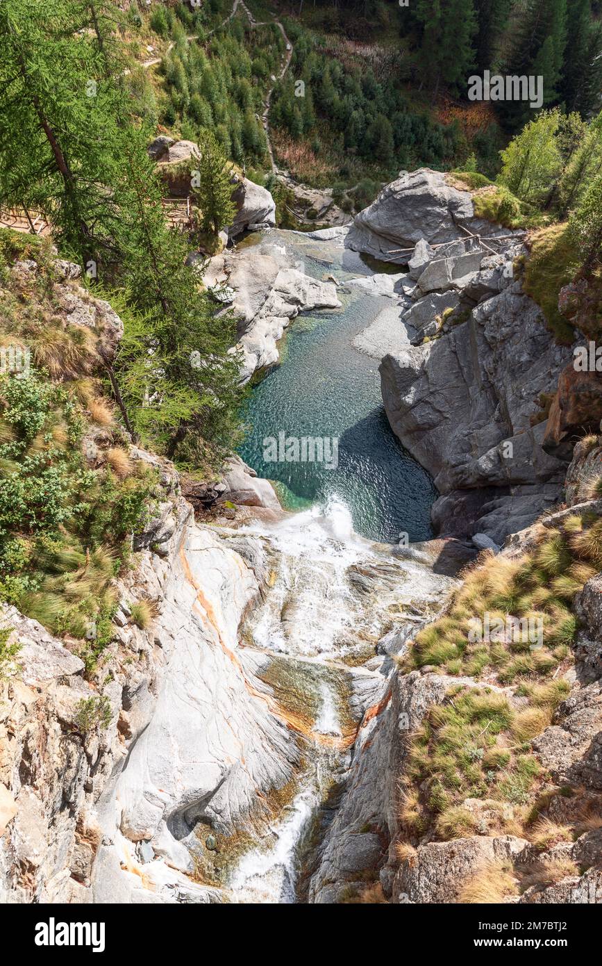 Blick von oben auf den Lillaz-Wasserfall (Cascate di Lillaz) und den smaragdgrünen Teich darunter, Felsen umgeben von grün-gelber Herbstvegetation Stockfoto