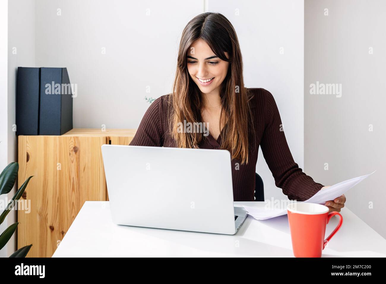 Lächelnde junge Erwachsene Frau, die zu Hause an einem Notebook arbeitet Stockfoto