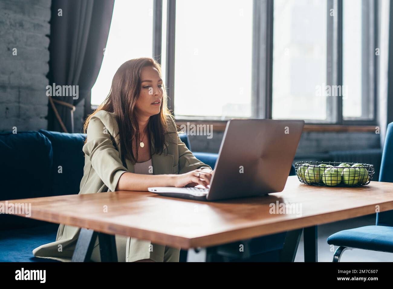 Die Frau zu Hause sitzt an ihrem Schreibtisch und schaut auf ihren Laptop-Bildschirm. Stockfoto