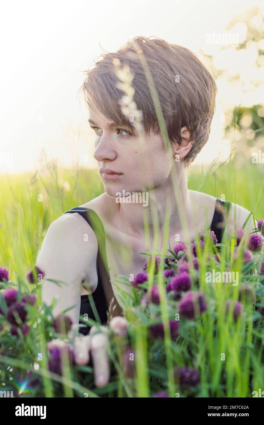Nahaufnahme einer aufmerksamen Dame, die auf einem Porträtbild mit frischem Gras sitzt Stockfoto