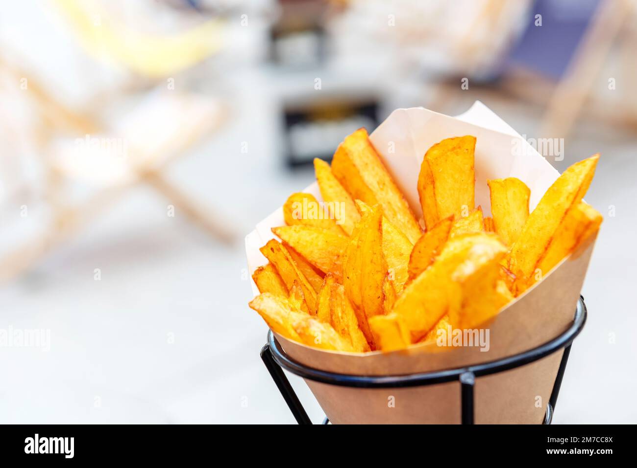 Im Ofen gebackene Kartoffelsplitter mit Meersalz und Kräutern. Pommes Frites in einer recycelbaren Papiertüte auf einem verschwommenen Straßenhintergrund, beliebtes Fast Street Food Stockfoto