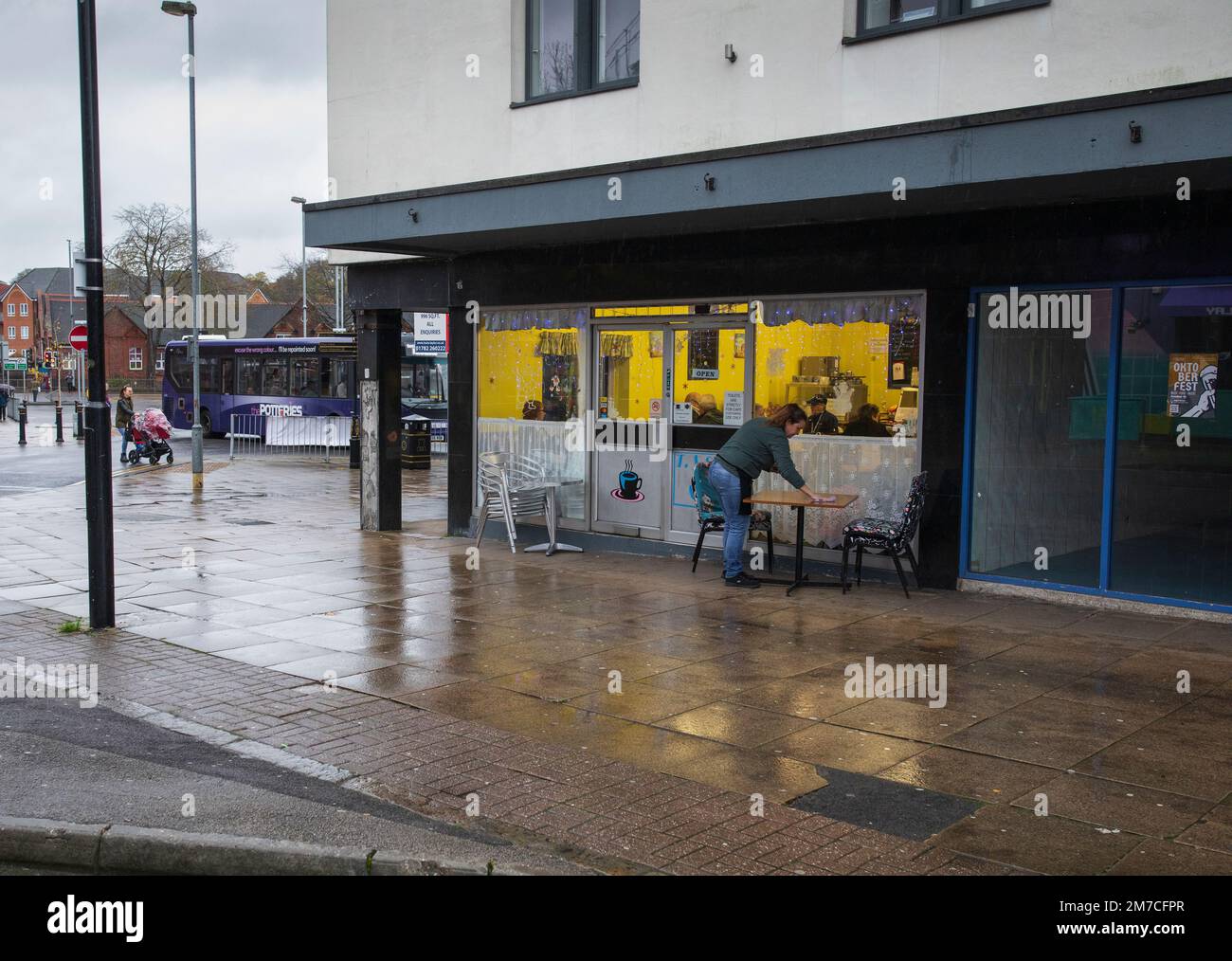 Eine Frau, die vor einem Café in Newcastle-under-Lyme, Staffordshire, Großbritannien, einen Tisch abwischt Stockfoto