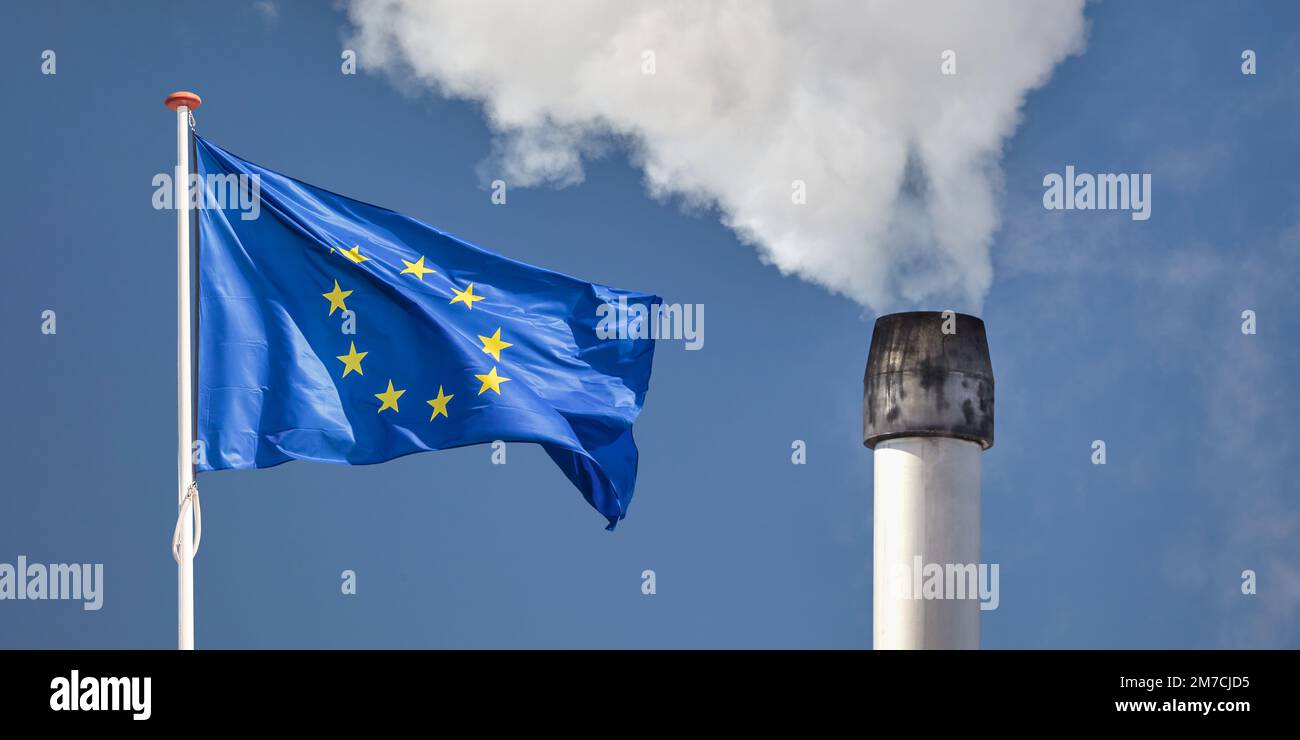 Vor einem verschmutzenden Fabrikschornstein mit Rauch die europäische Flagge zu schwenken Stockfoto