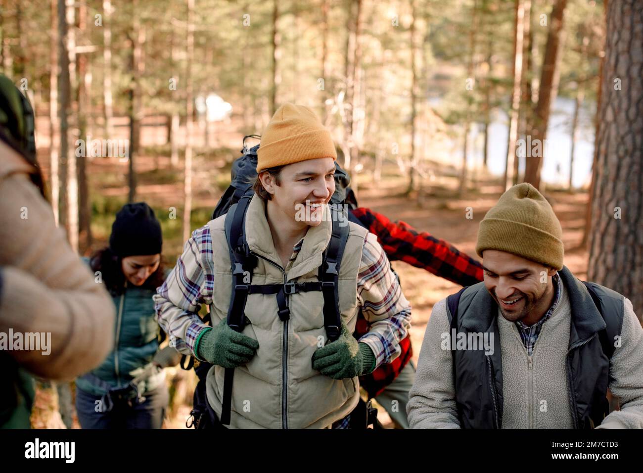 Glücklicher junger Mann, der mit einem männlichen Freund spricht, während er im Wald wandert Stockfoto