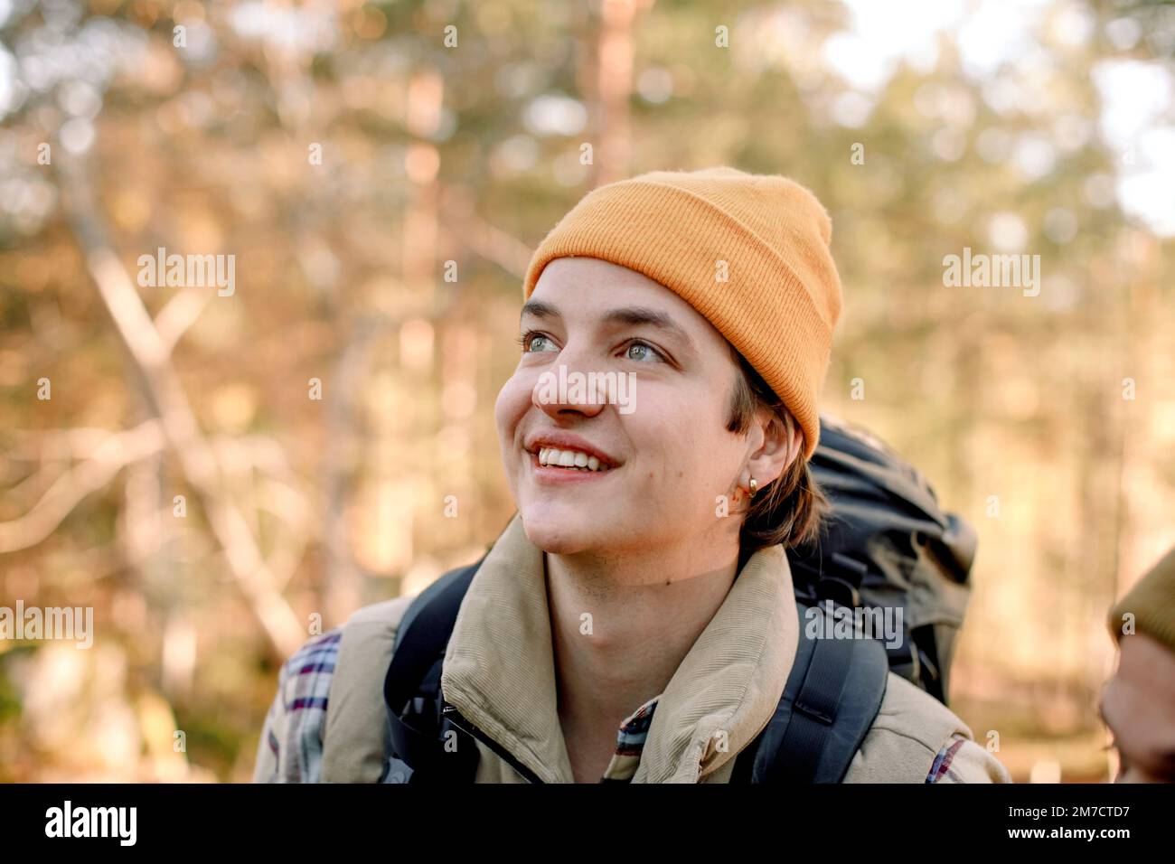 Ein junger lächelnder Mann mit Strickmütze, der beim Wandern wegschaut Stockfoto