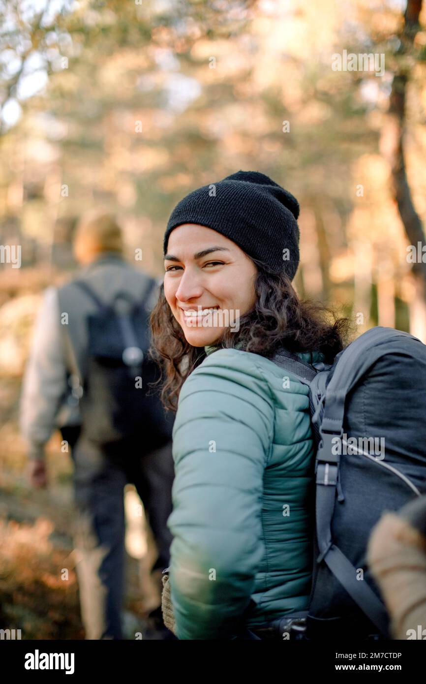 Glückliche Frau, die über die Schulter blickt, während sie im Wald wandert Stockfoto